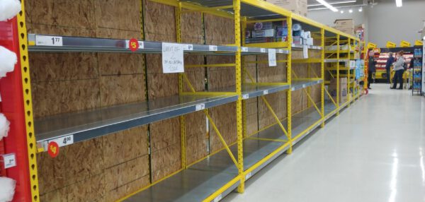Several metres of grocery shelving that are bare, except for a sign asking customer not to buy more than two packages of toilet paper.